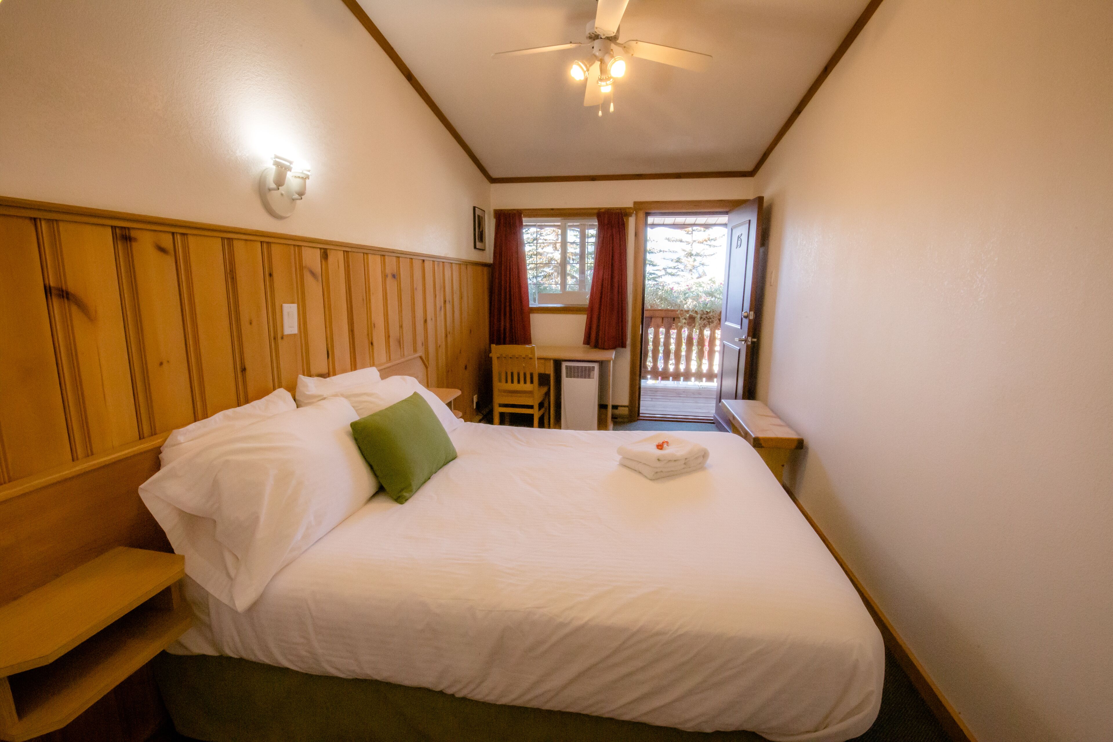 Une chambre d’hôtel avec un lit, un bureau, une chaise et un balcon.