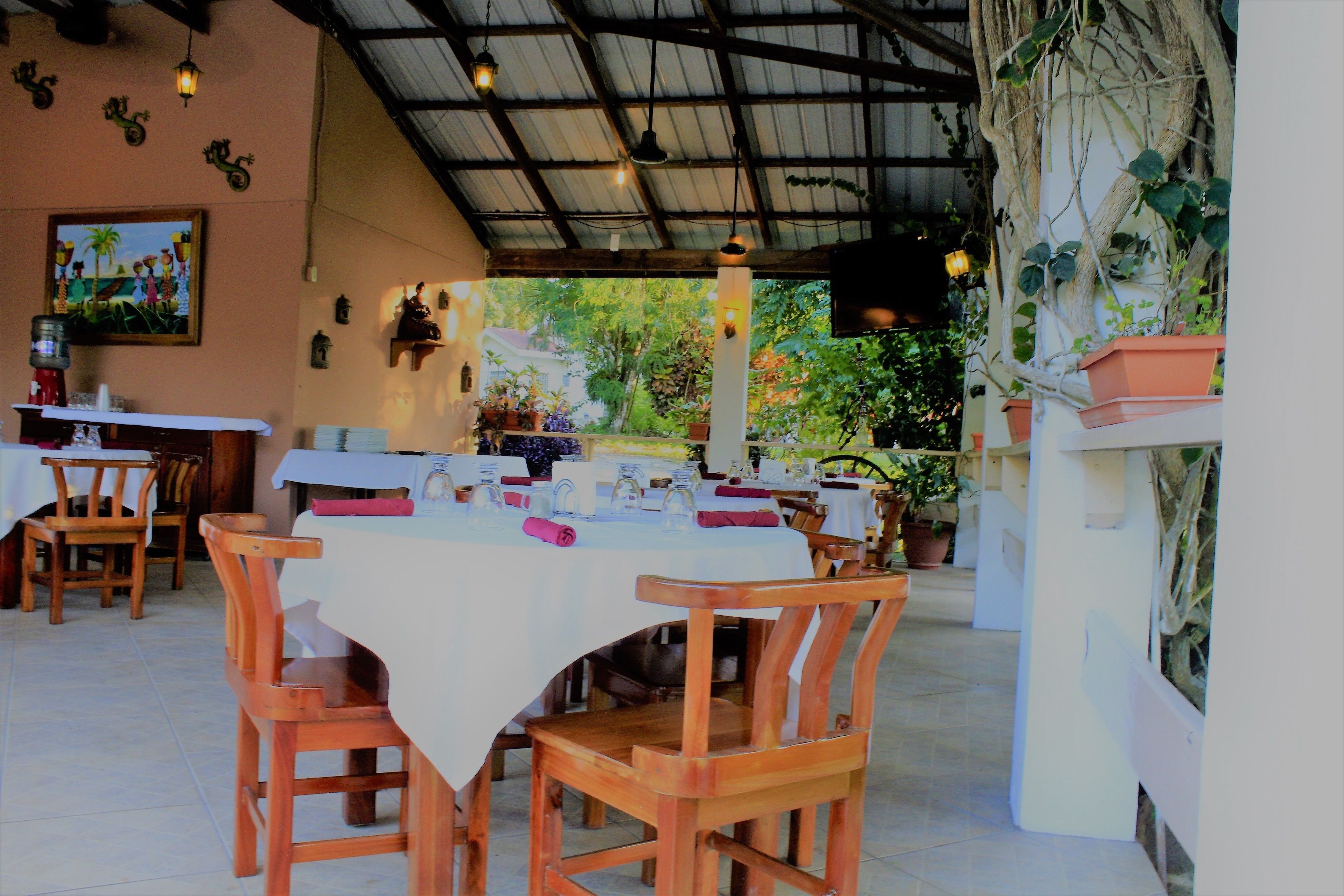 An outdoor dining area with wooden tables and chairs, a covered roof, and potted plants.