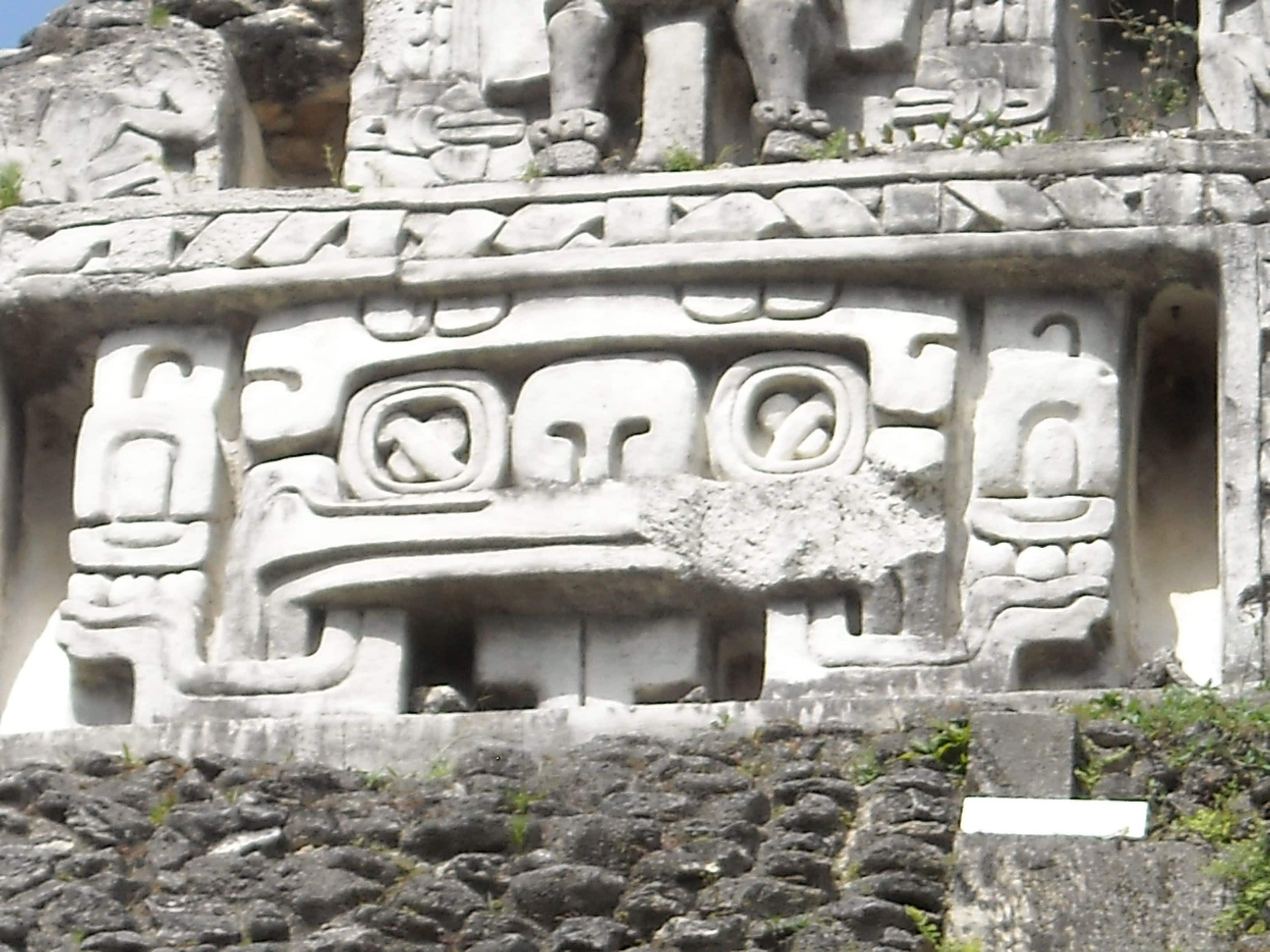 Una struttura in pietra con elaborate sculture, tra cui una figura centrale con un copricapo e una figura più piccola a sinistra.