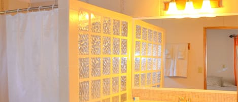 Un baño con techo de madera, cortina de ducha, lavabo con espejo y piso de baldosas.