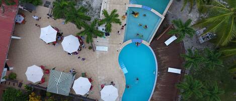 Vista aérea de un resort con varias piscinas, tumbonas y palmeras.