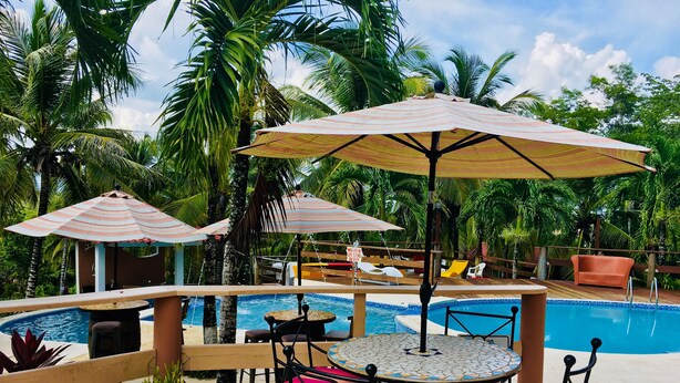 A poolside area with a tiled deck, a round table with chairs, and striped umbrellas.