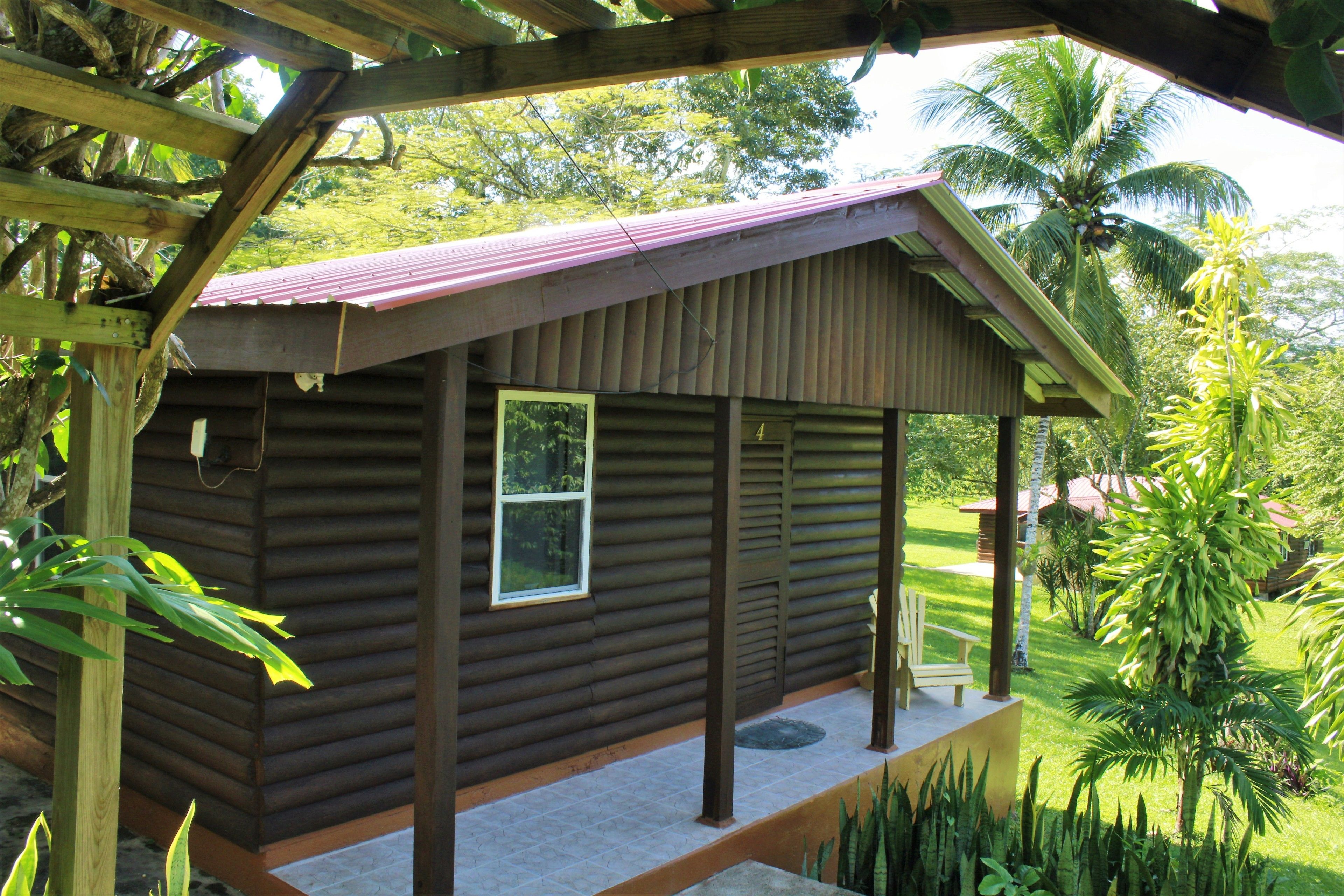 A wooden cabin with a porch, surrounded by lush greenery and palm trees.
