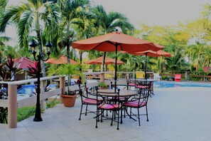 A poolside area with outdoor seating, umbrellas, and palm trees.