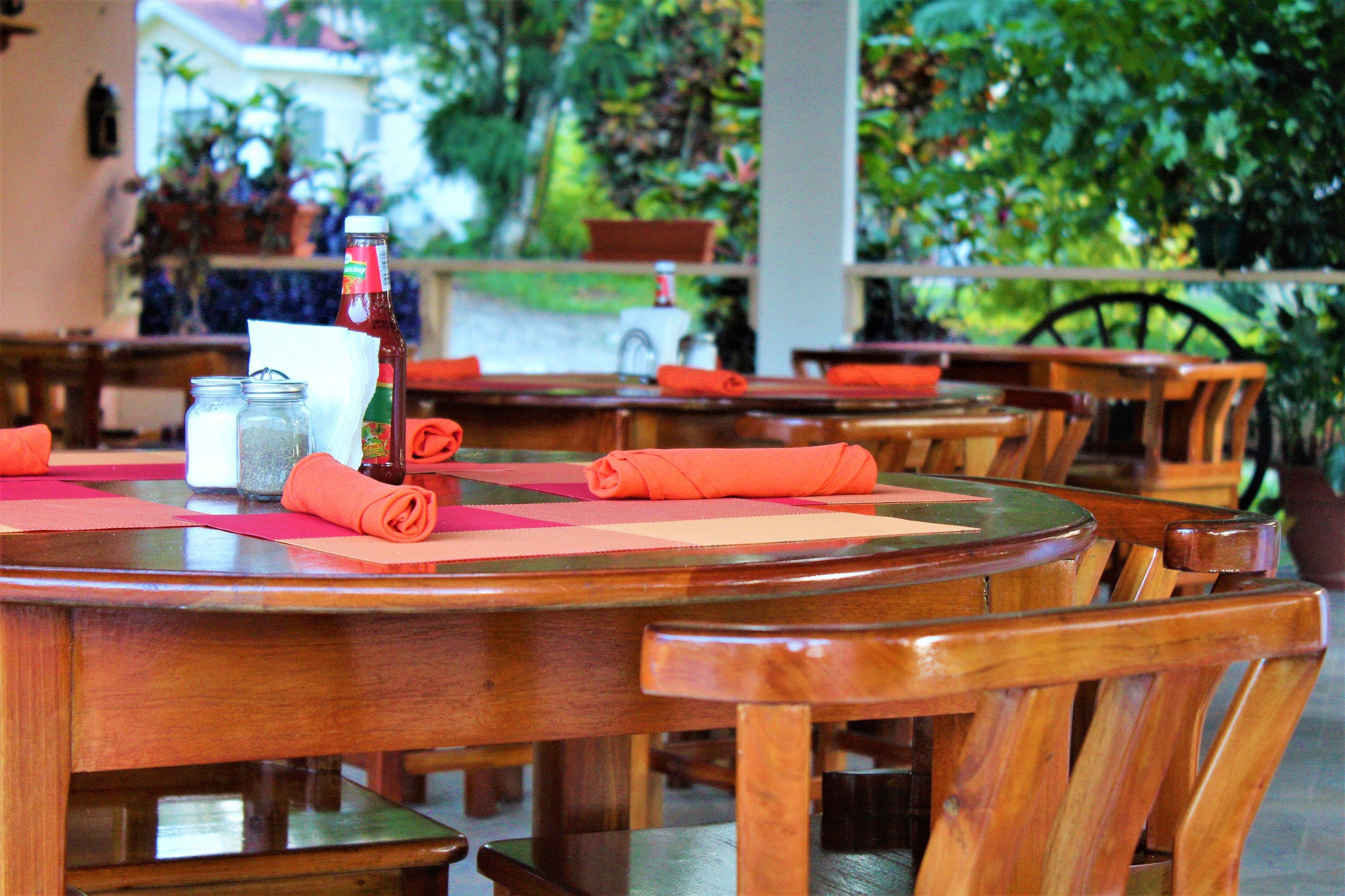 A restaurant with wooden tables and chairs, a bottle of ketchup, and a salt shaker on the tables.