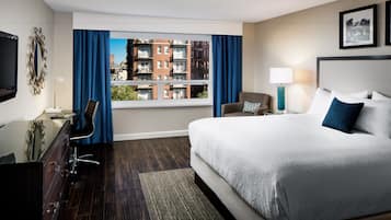 Une chambre d’hôtel avec un grand lit, un bureau avec une chaise, une télévision, une fenêtre avec des rideaux et une vue sur les bâtiments.