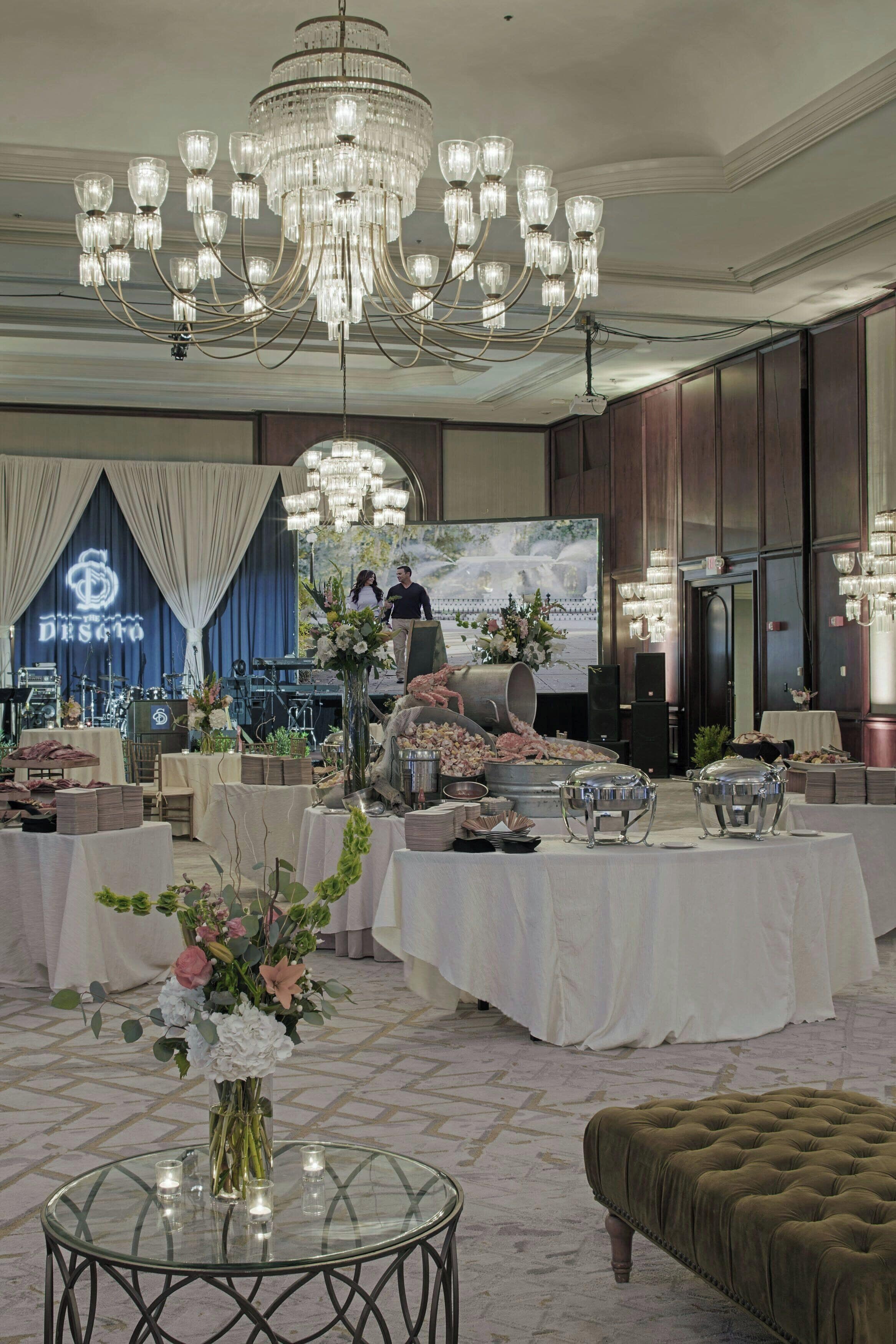 A banquet hall with a large chandelier, tables set for a formal event, and a stage with a backdrop.