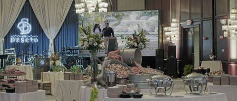 A banquet hall with a large chandelier, tables set for a formal event, and a stage with a backdrop.