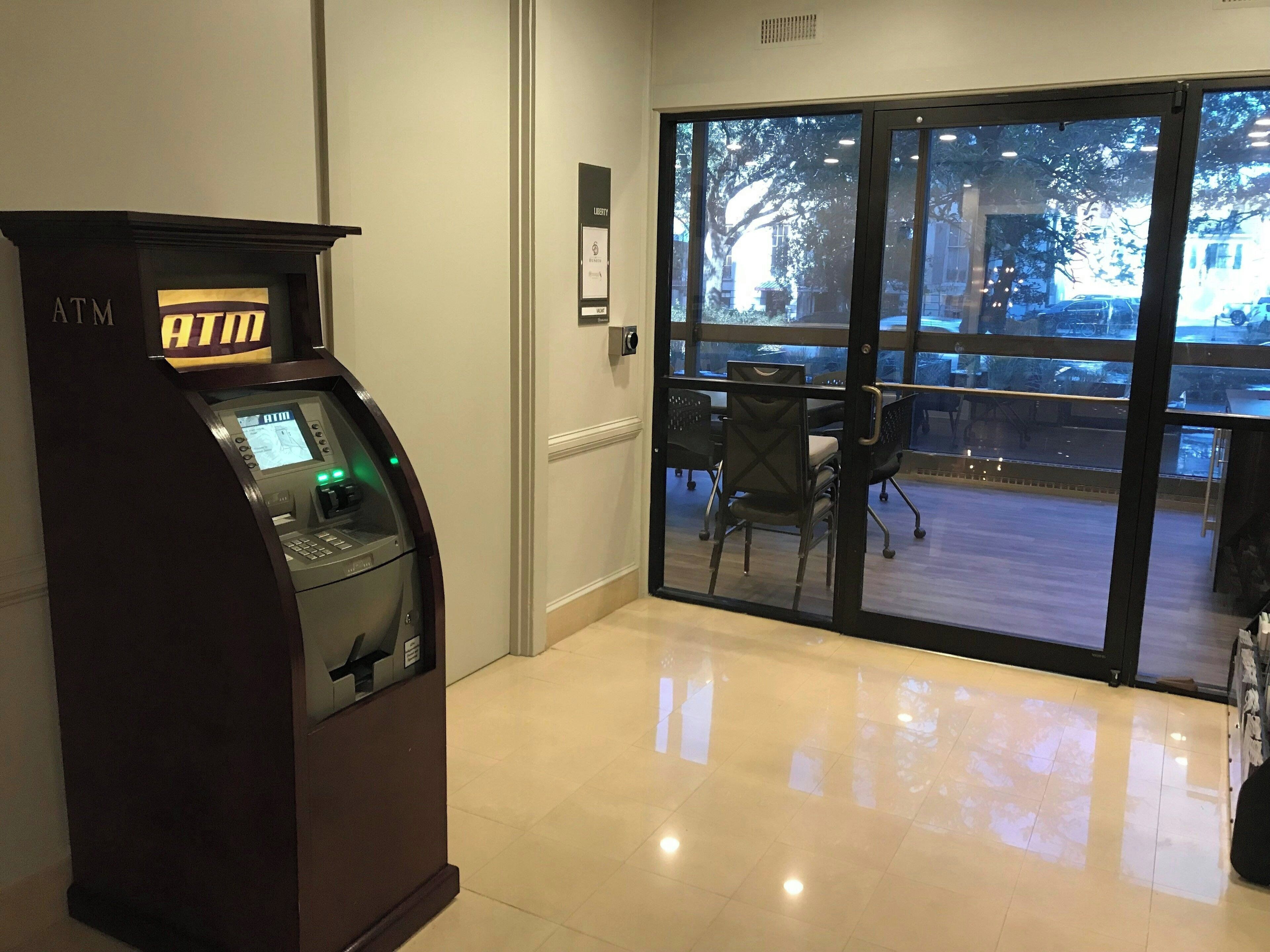 An ATM machine in a lobby with a glass door leading outside.