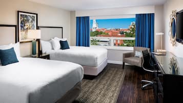 A hotel room with two beds, a desk, a chair, a TV, and a window with a city view.