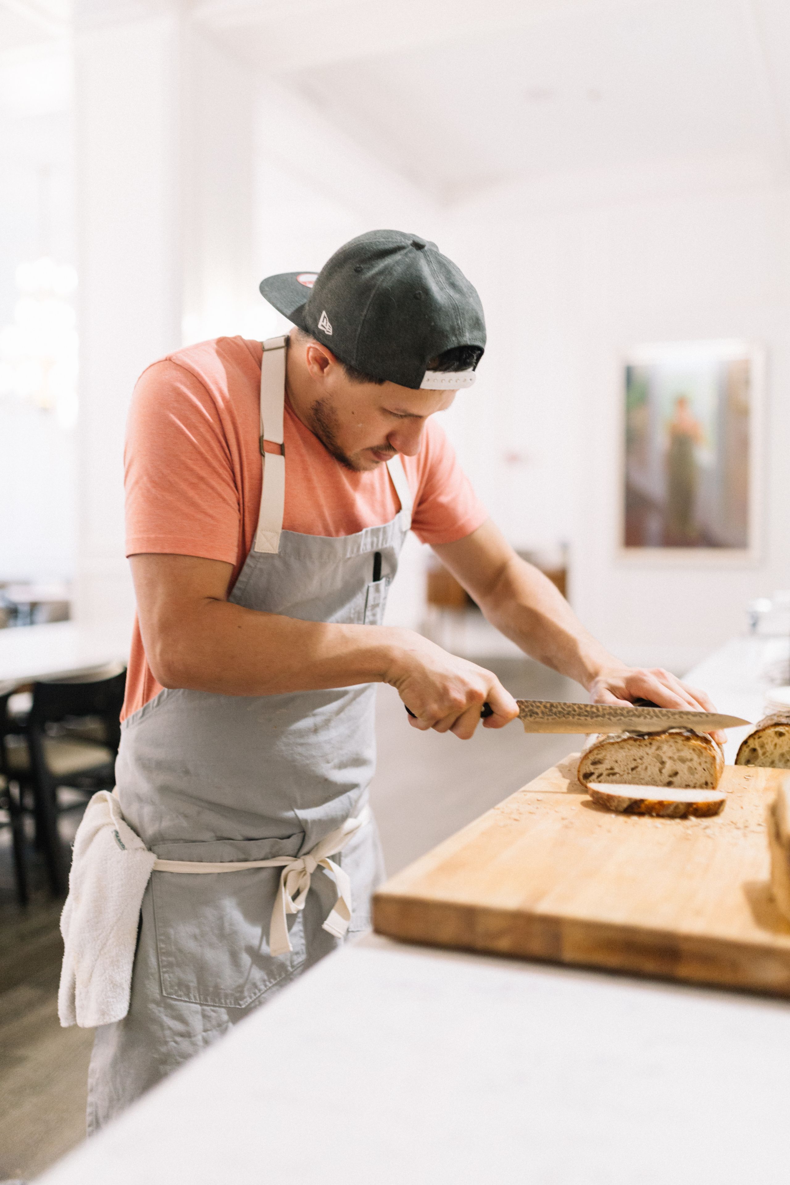 A person cutting bread on a wooden cutting board in a kitchen.