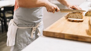 A person cutting bread on a wooden cutting board in a kitchen.