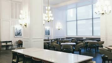 A spacious dining area with a long table and multiple chairs, large windows, and chandeliers.