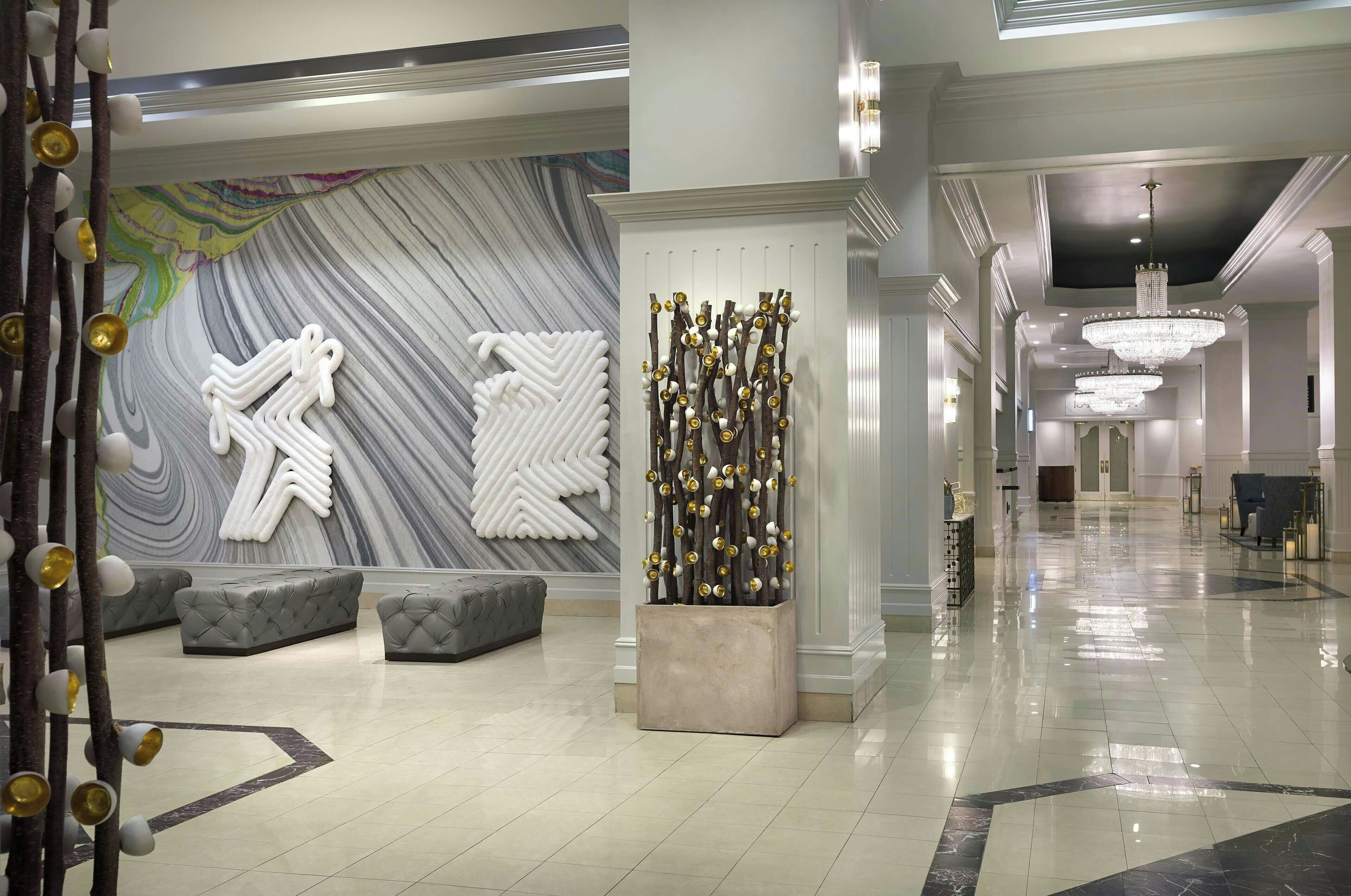 A hotel lobby with a marble wall, a decorative tree, and a chandelier.