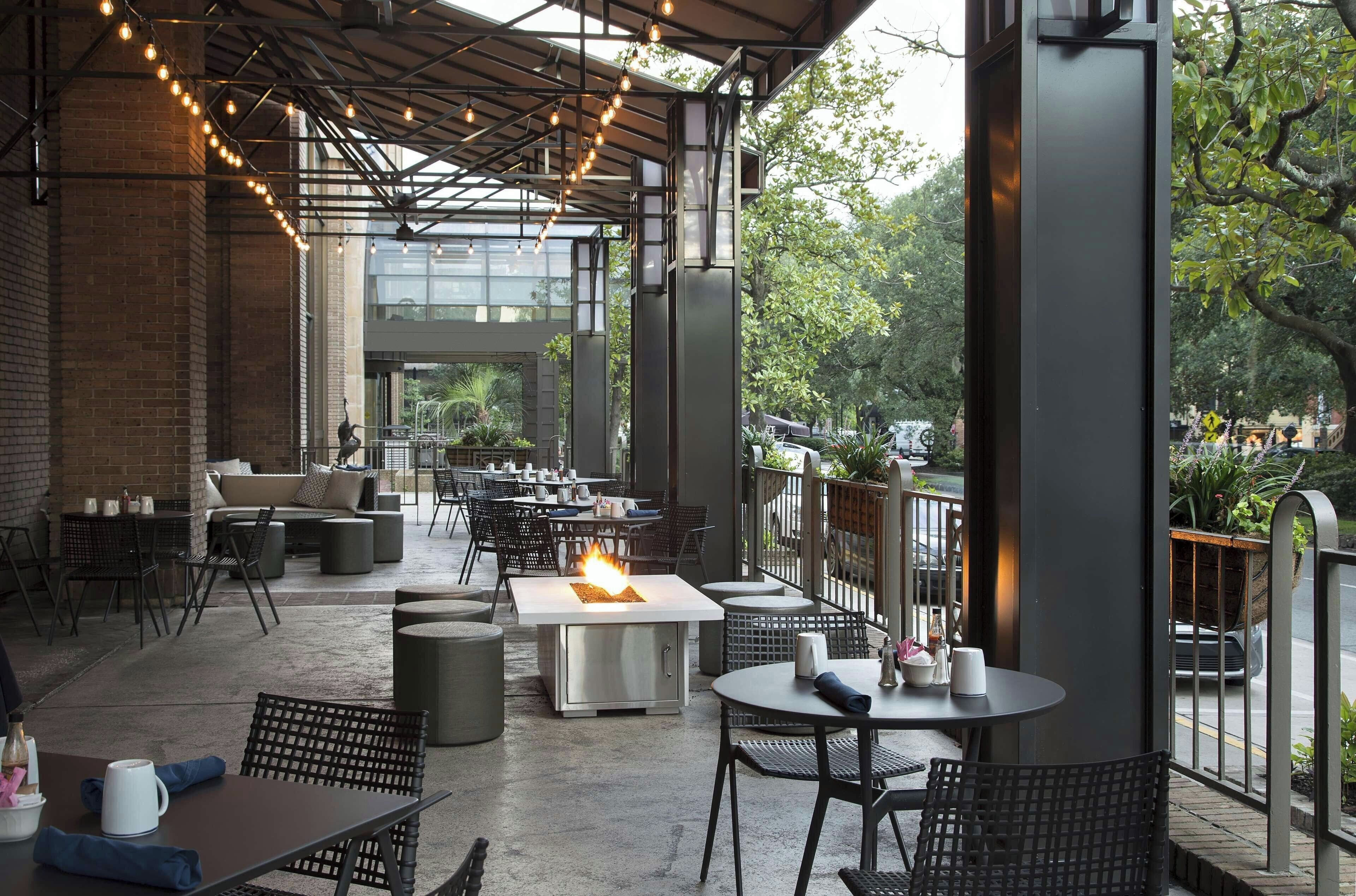 An outdoor patio area with tables and chairs, a fire feature, and a view of the surrounding greenery.