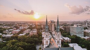 A church with two spires, surrounded by urban buildings and greenery.