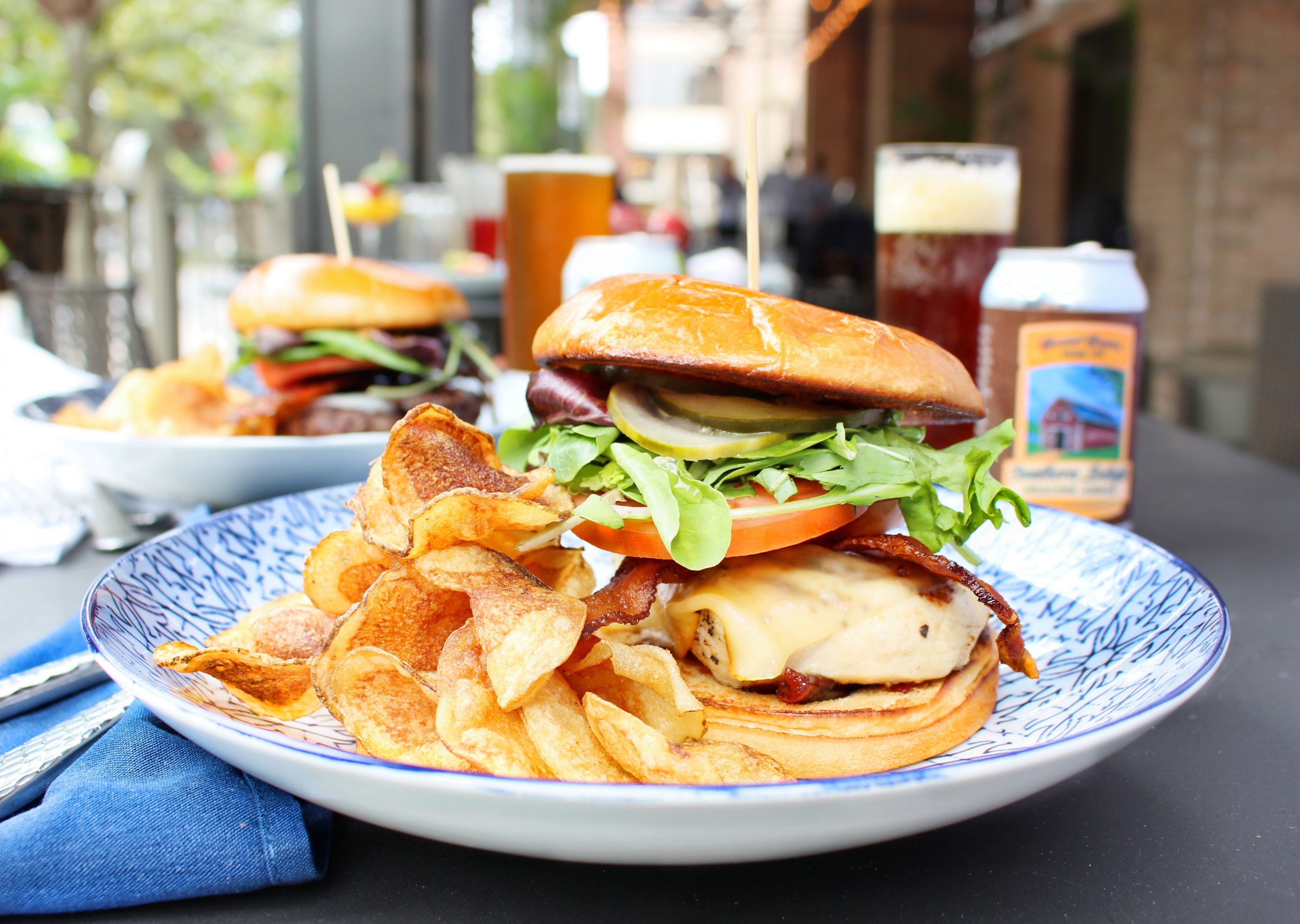 A plate with a burger, chips, and a drink on a table.