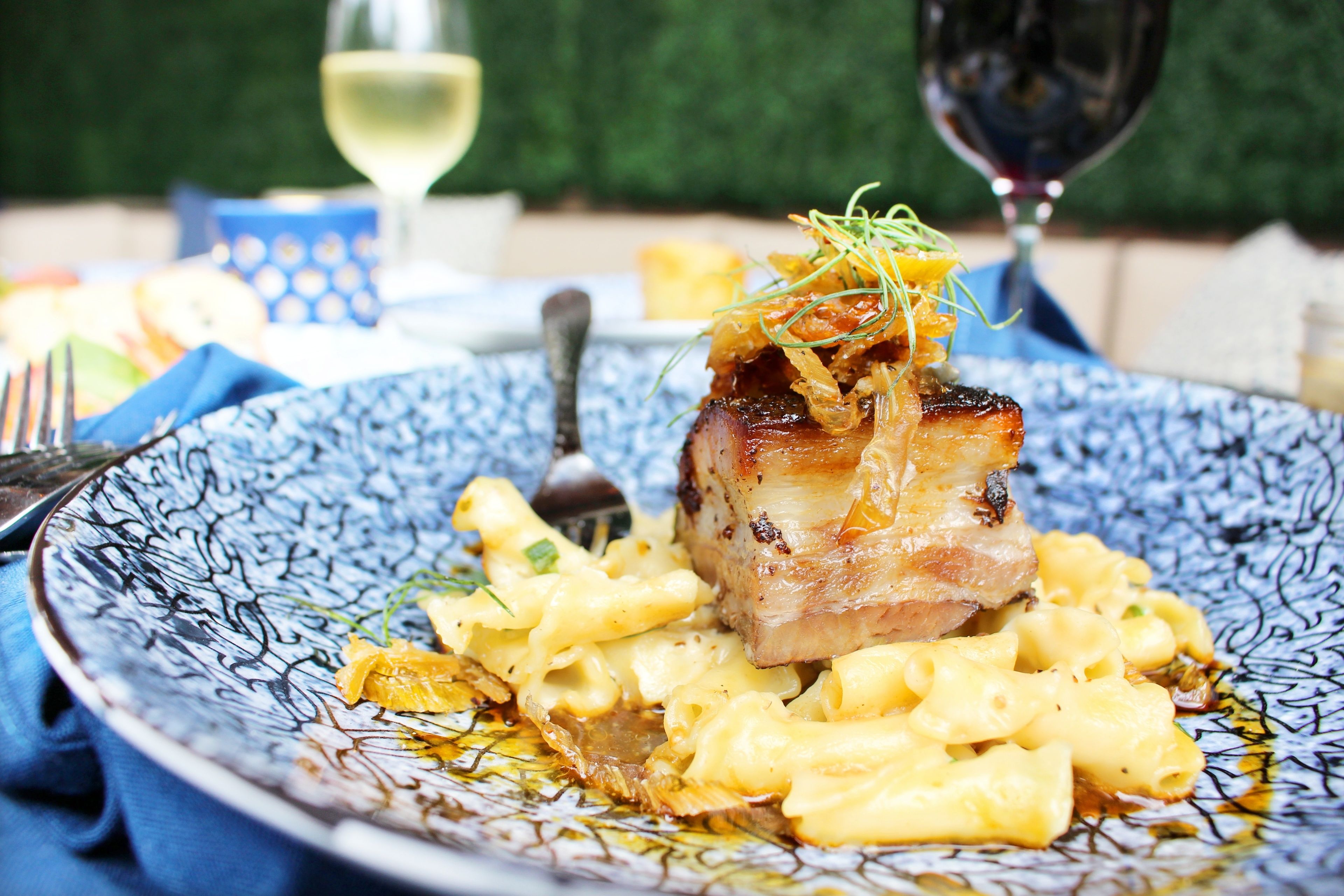 A plate of food with pasta and a piece of meat, accompanied by a glass of wine.