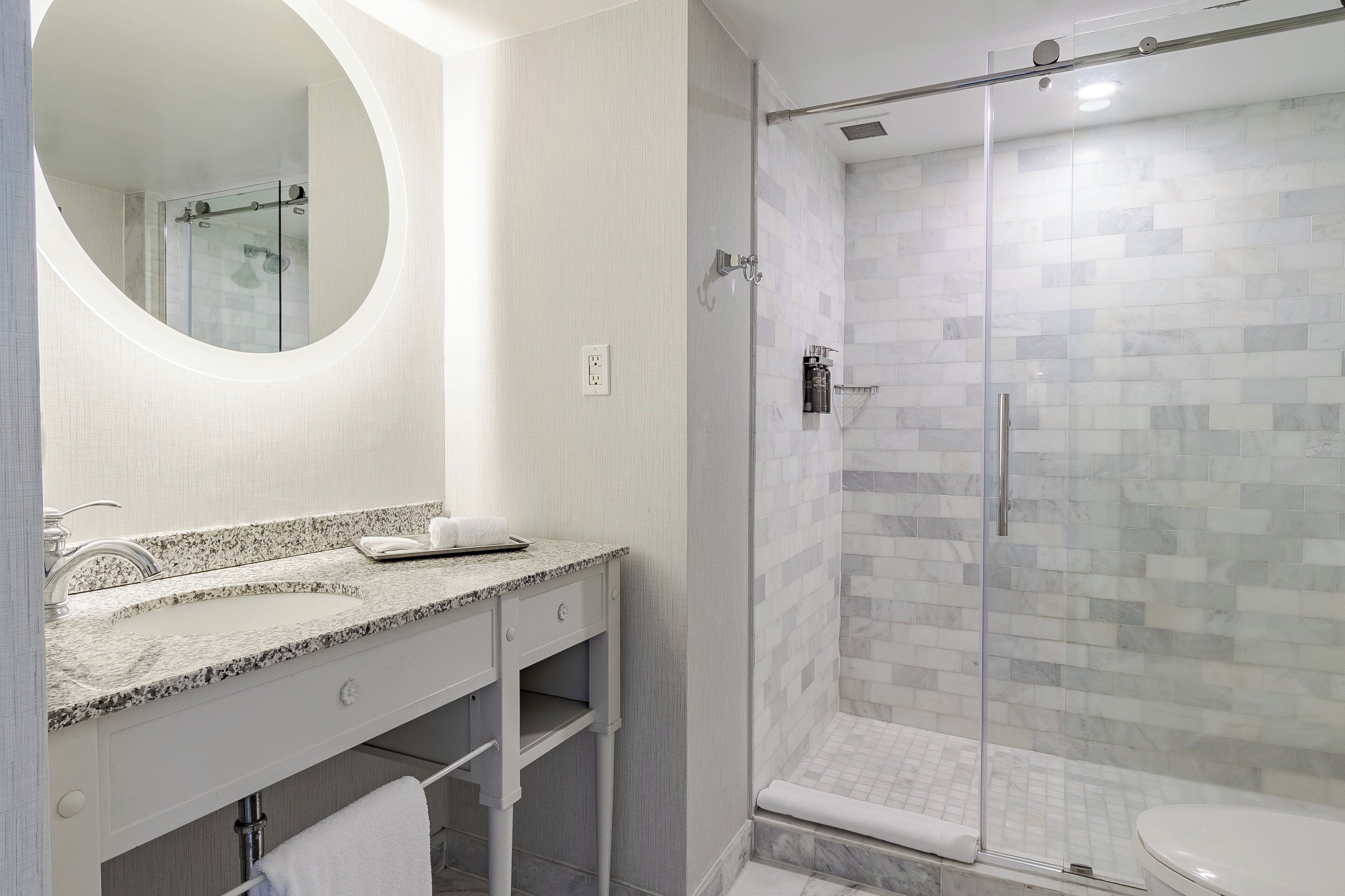 A modern bathroom with a glass-enclosed shower, a granite countertop sink, and a large mirror.