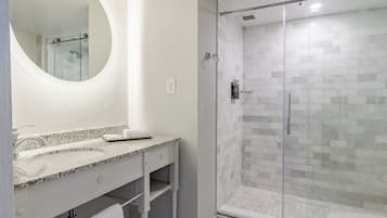 A modern bathroom with a glass-enclosed shower, a granite countertop sink, and a large mirror.