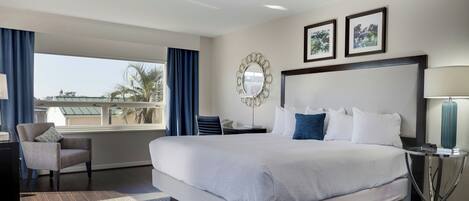 A hotel room with a large bed, a desk with a lamp, a chair, and a view of the outdoors.