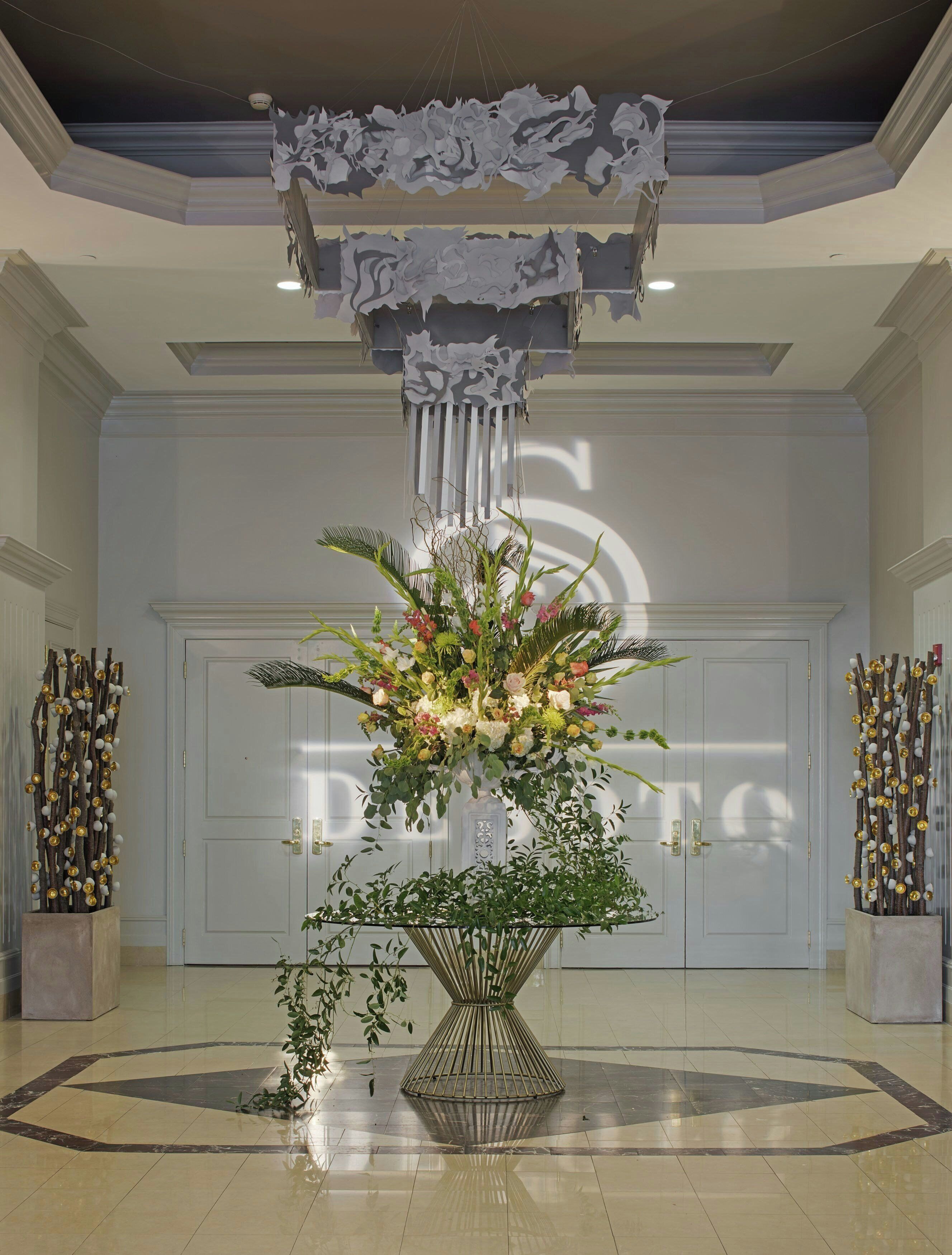 A lobby with a central floral arrangement, double doors, and decorative columns.