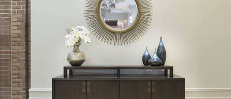 Une console en bois foncé, surmontée d’un miroir à cadre doré, et agrémentée de fleurs blanches et de deux vases bleus de chaque côté.