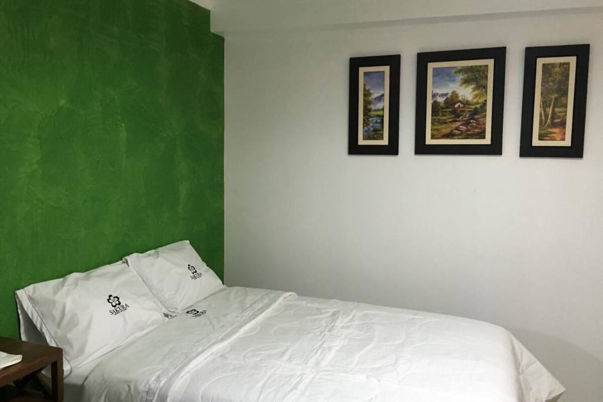 Una cama individual con ropa de cama blanca en una habitación con una pared de acento verde y tres cuadros en la pared.
