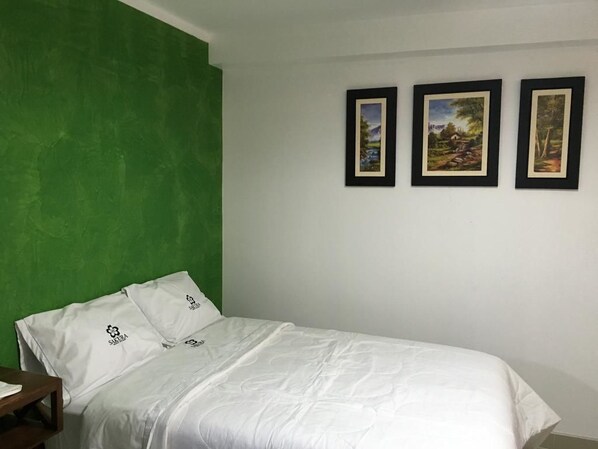 A single bed with white bedding in a room with a green accent wall and three framed pictures on the wall. - Sakura River Hotel (Bagua Grande)