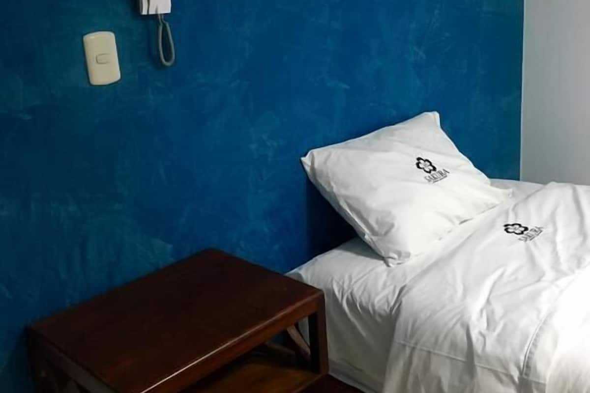 Una habitación con pared azul con textura, una mesita de noche de madera, una cama con ropa blanca y un teléfono.