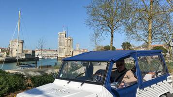 A vintage white and blue car parked near a waterfront with a castle in the background.