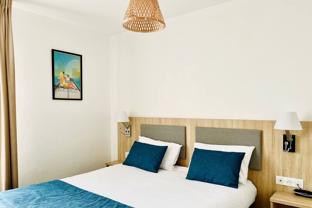 Habitación de hotel con cama, dos lámparas de noche, una mesita de noche, un enchufe y una lámpara de pared.
