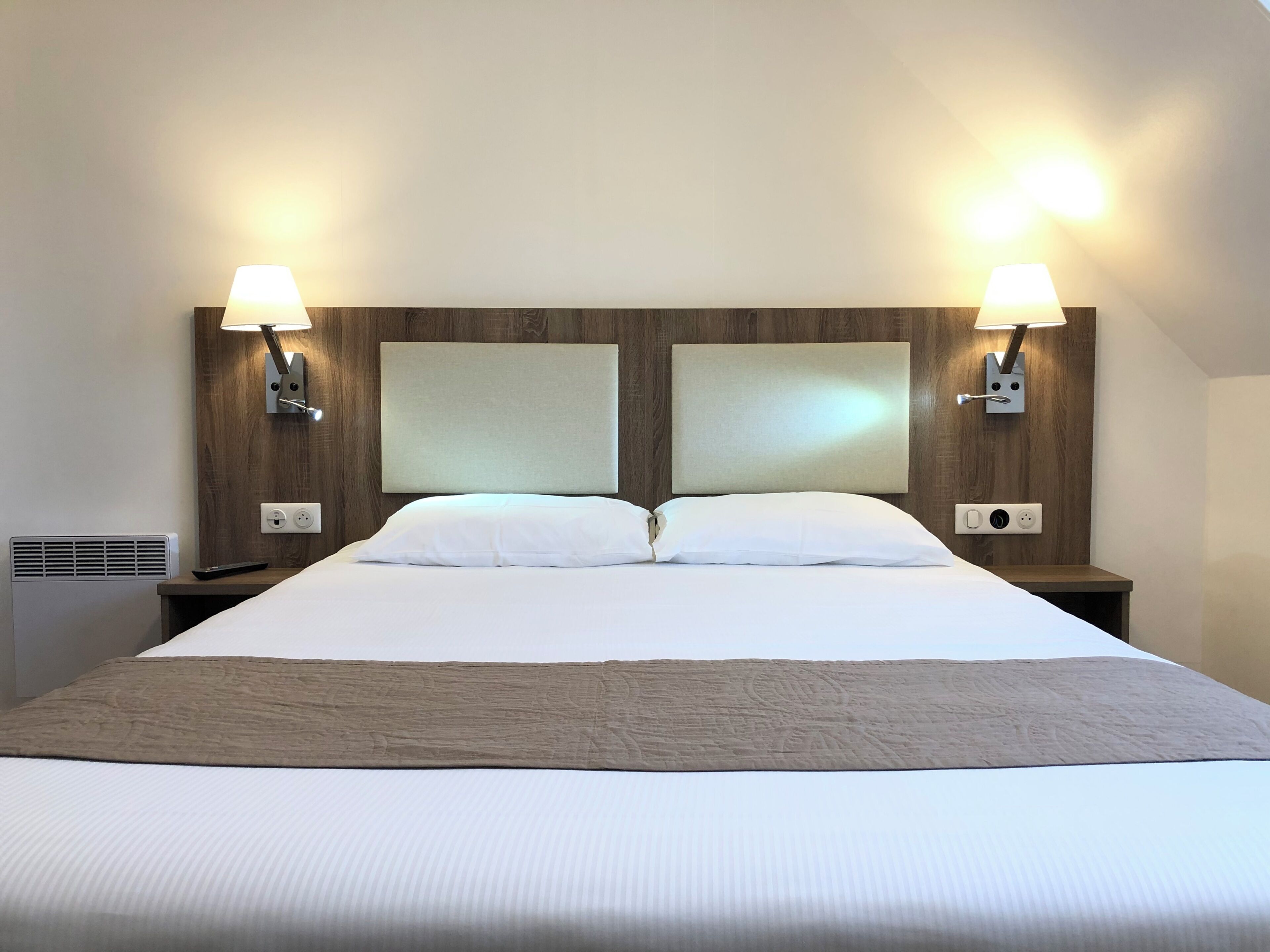 Habitació d'hotel amb un llit gran, dues làmpades de nit, un reposacapses i una presa elèctrica.