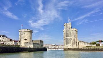 Un castillo de piedra histórico con dos torres, una bandera y un cuerpo de agua al frente.