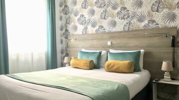 A hotel room with a bed, two pillows, a bedside table with a lamp, and a wall with a leaf pattern.