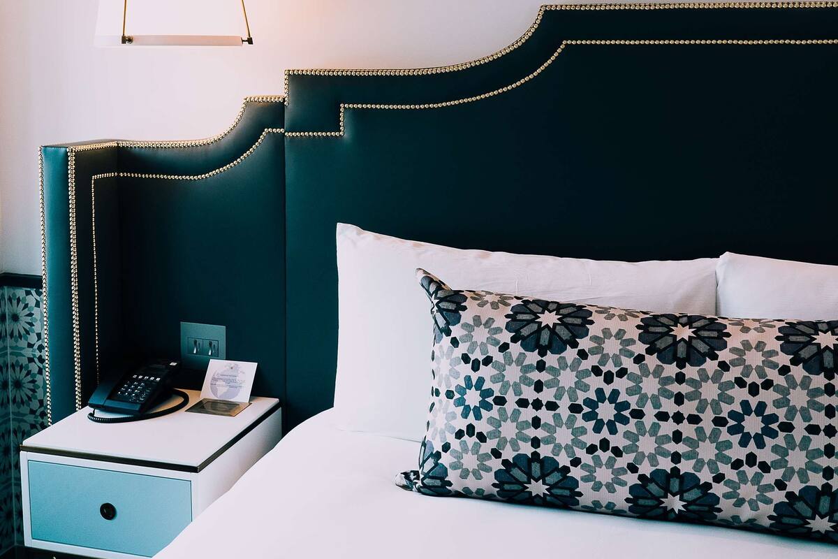 A neatly made bed with patterned pillows, a bedside table with a phone and a lamp, and a dark headboard.
