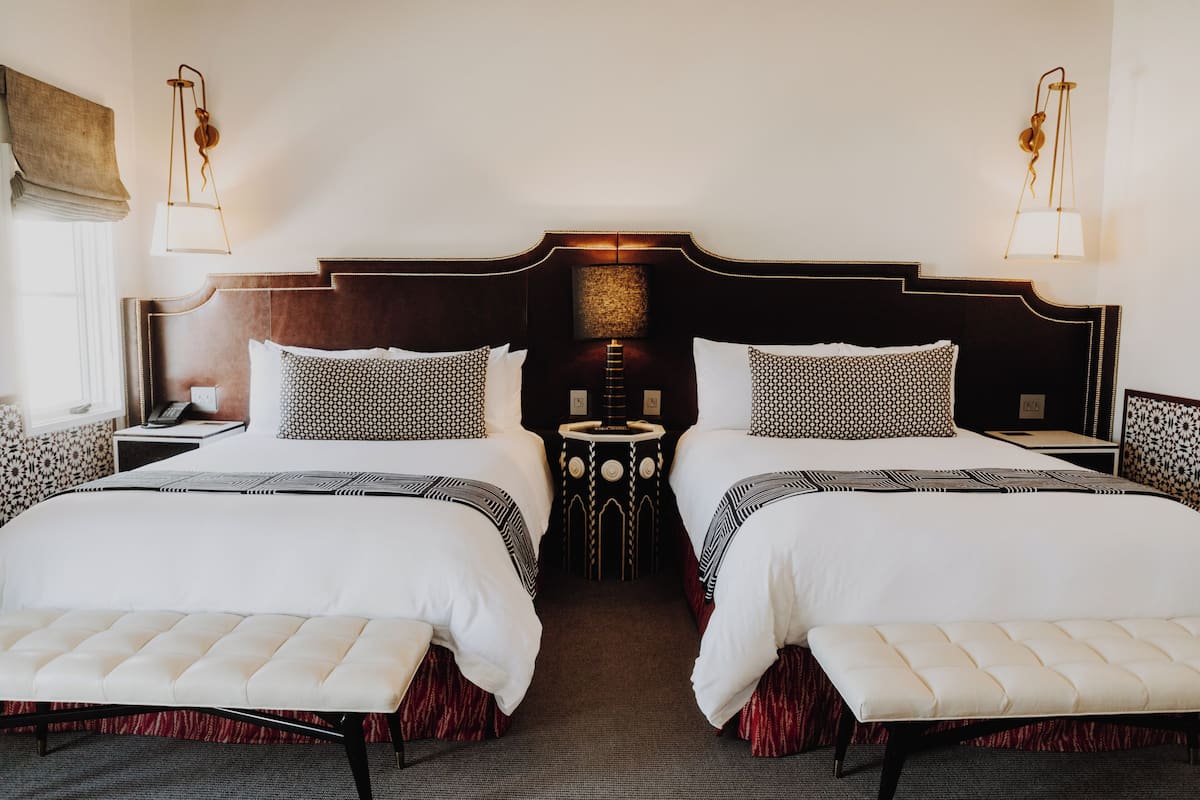 A hotel room with two beds, a small round table, and a bench.