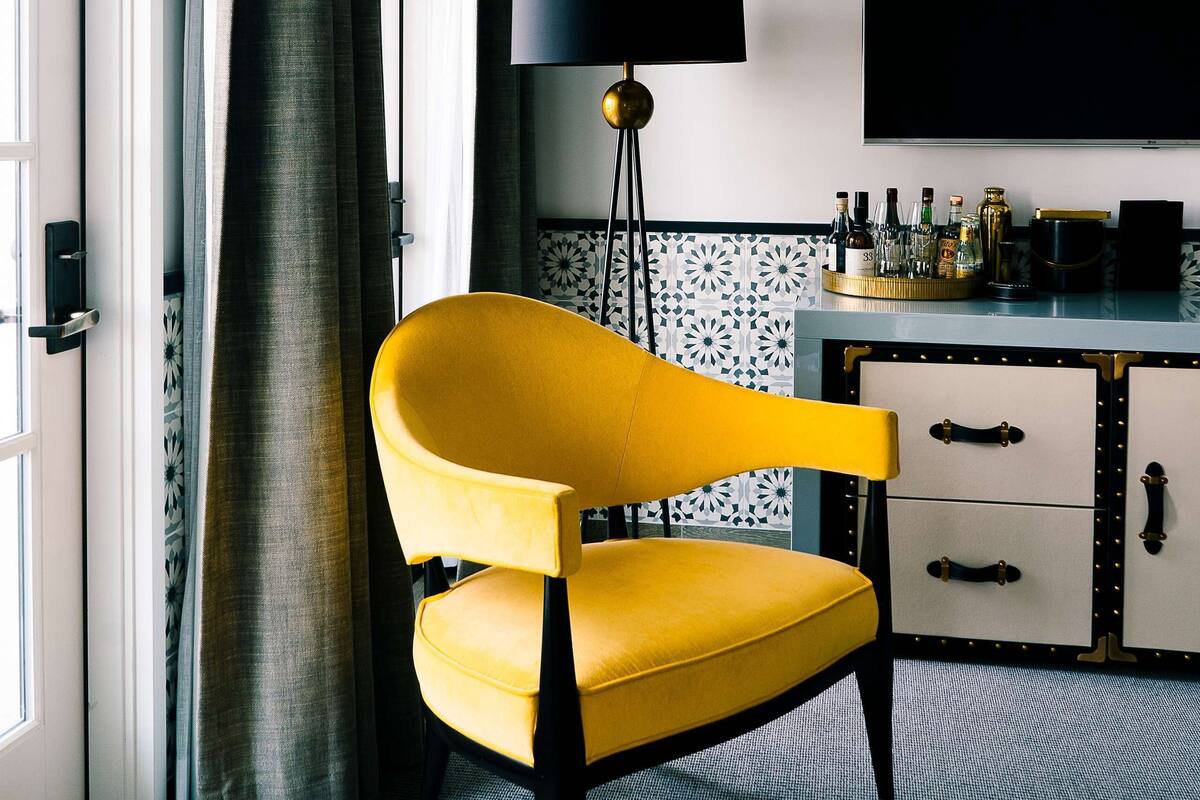 A room with a yellow armchair, a black floor lamp, a flat-screen TV, and a minibar.