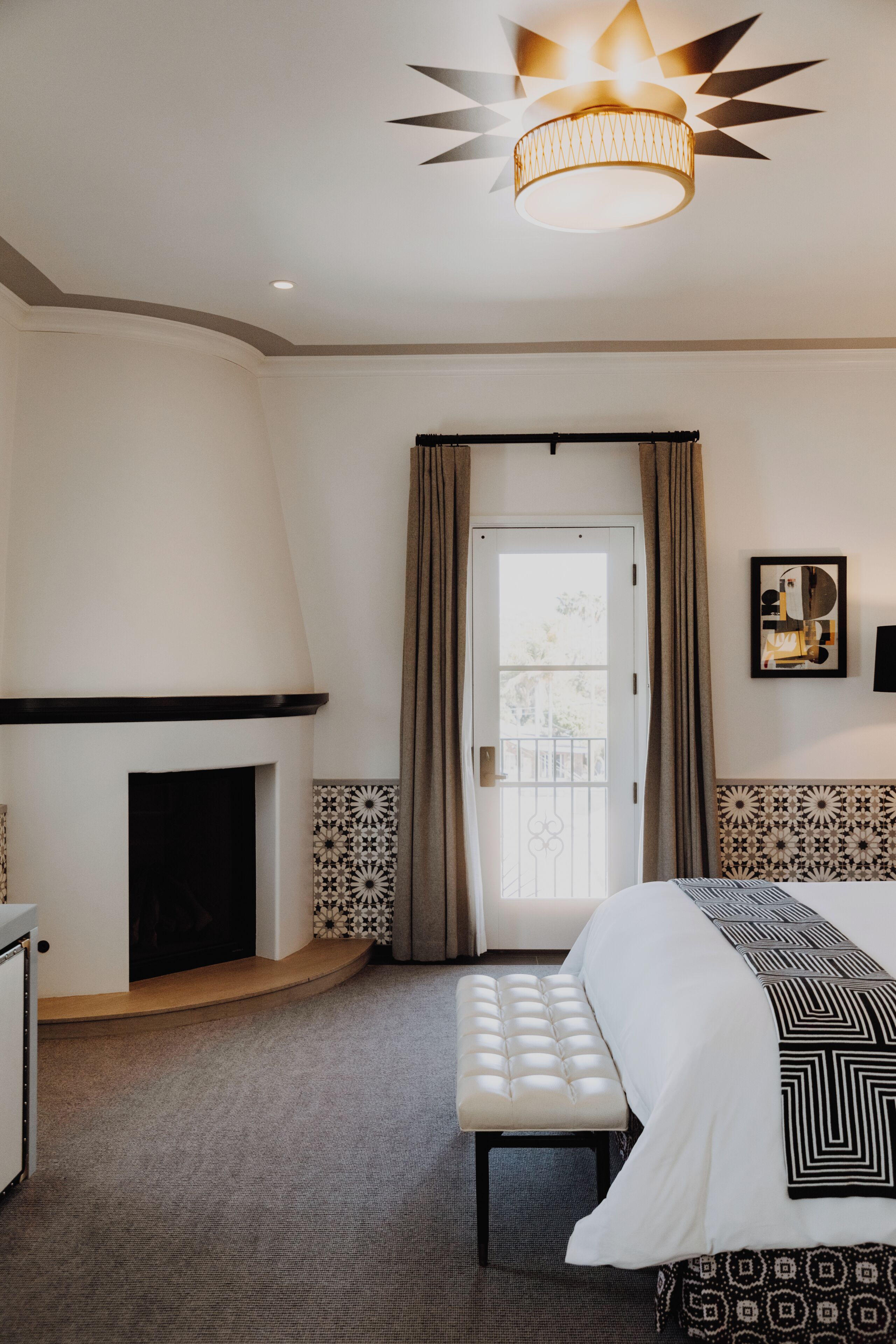 Habitación de hotel con cama, banco, chimenea y lámpara en el techo.