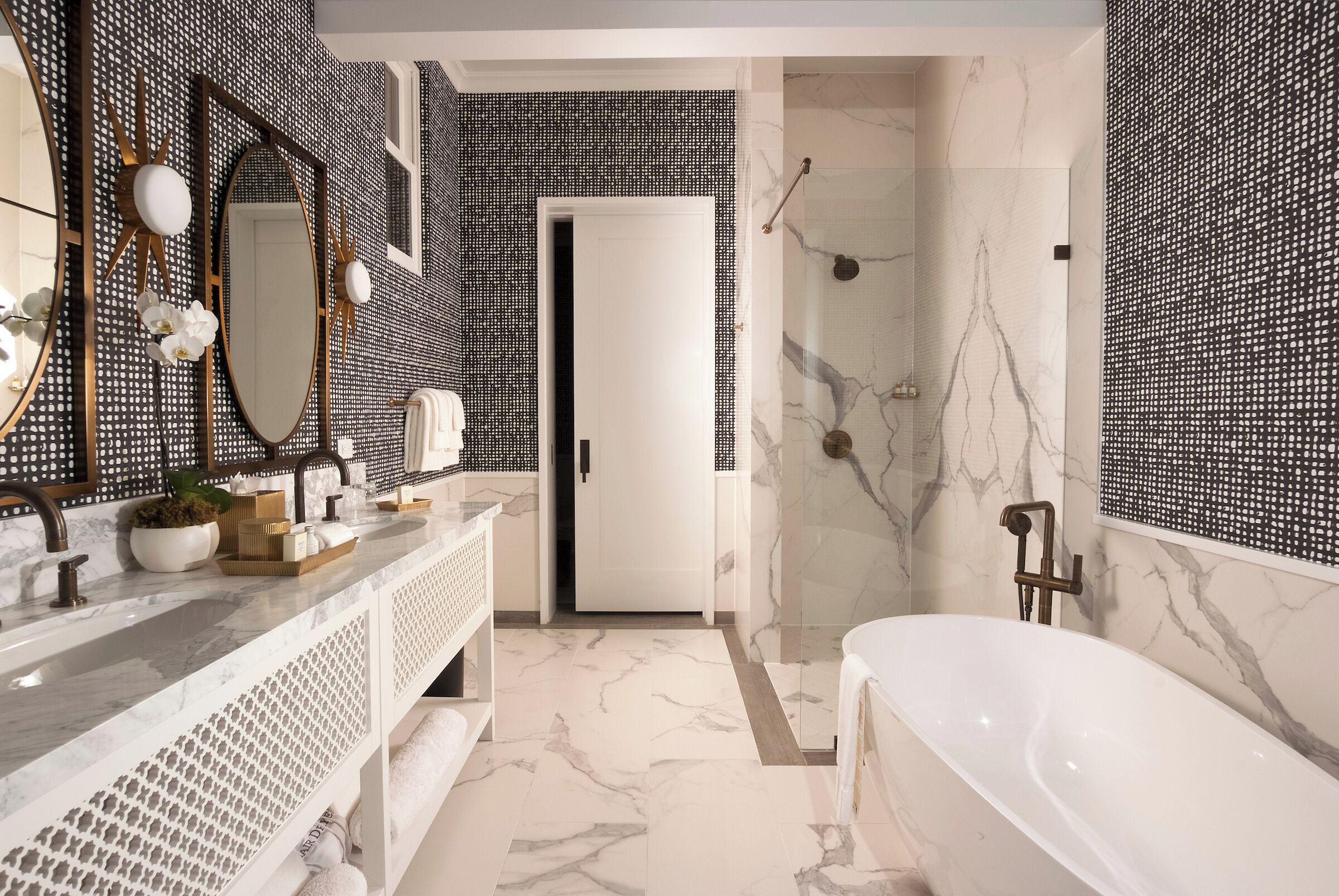 A modern bathroom with a marble floor, a freestanding bathtub, and a large mirror with decorative elements.