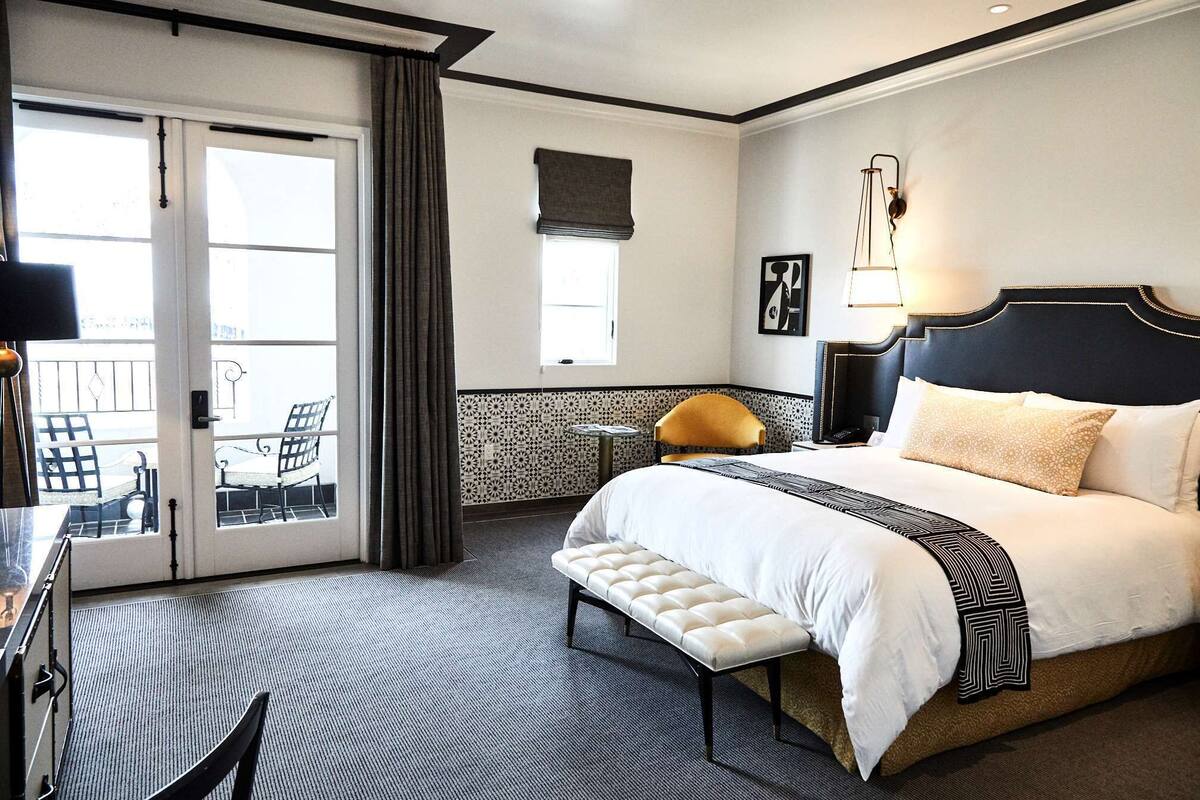 A hotel room with a large bed, a bench, a desk, and a view of the outside balcony.