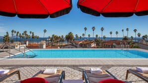 A pool area with lounge chairs and umbrellas, a clear view of the ocean, and palm trees. - Hotel Californian (Santa Barbara)