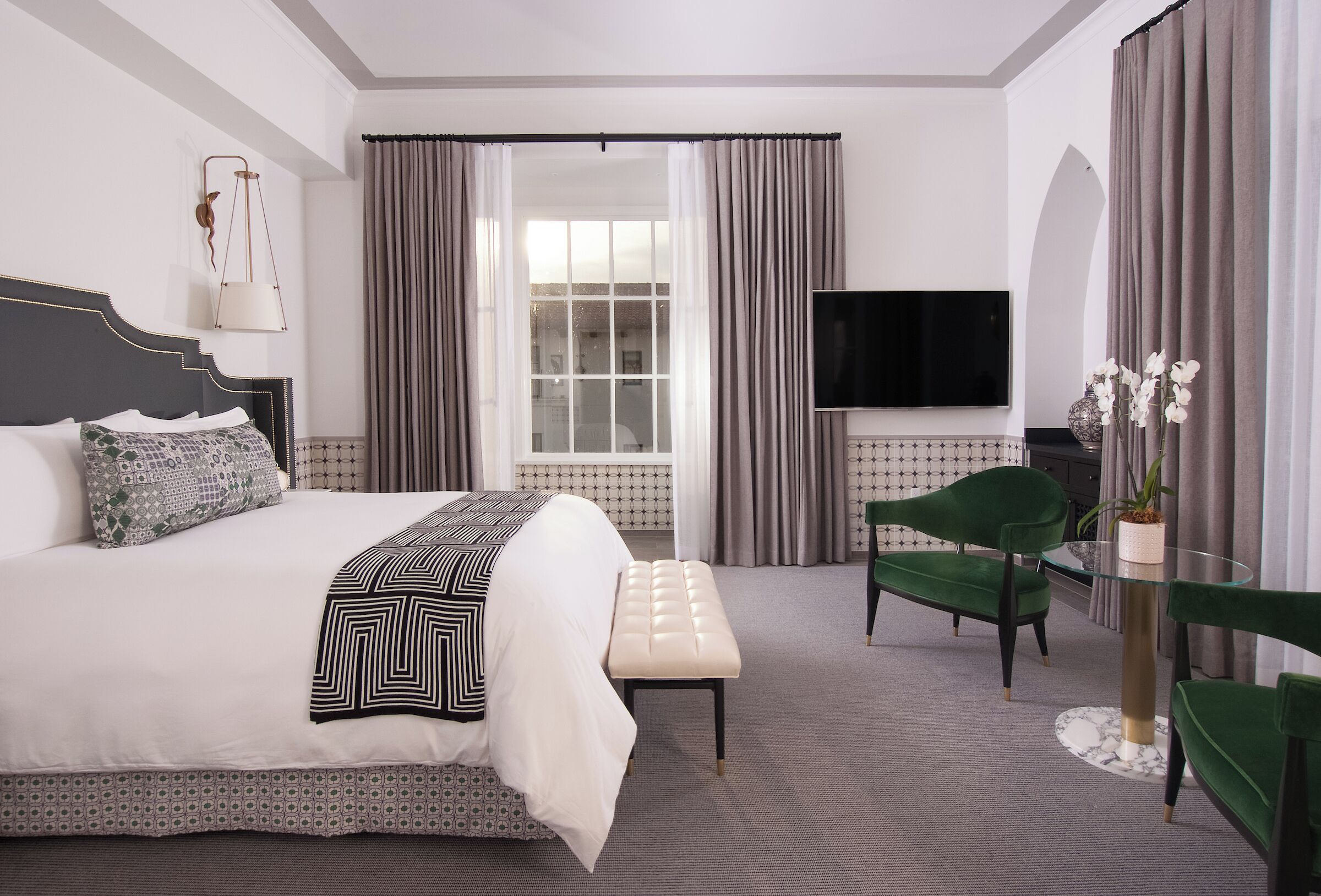 A hotel room with a bed, a television, a green chair, and a small table.