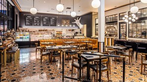 A restaurant interior with hexagonal patterned flooring, wooden tables and chairs, a bar area with a counter, and a menu board on the wall. - Hotel Californian (Santa Barbara)
