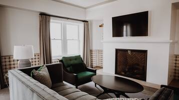 A living room with a sofa, armchair, and table, a fireplace, and a TV mounted on the wall.