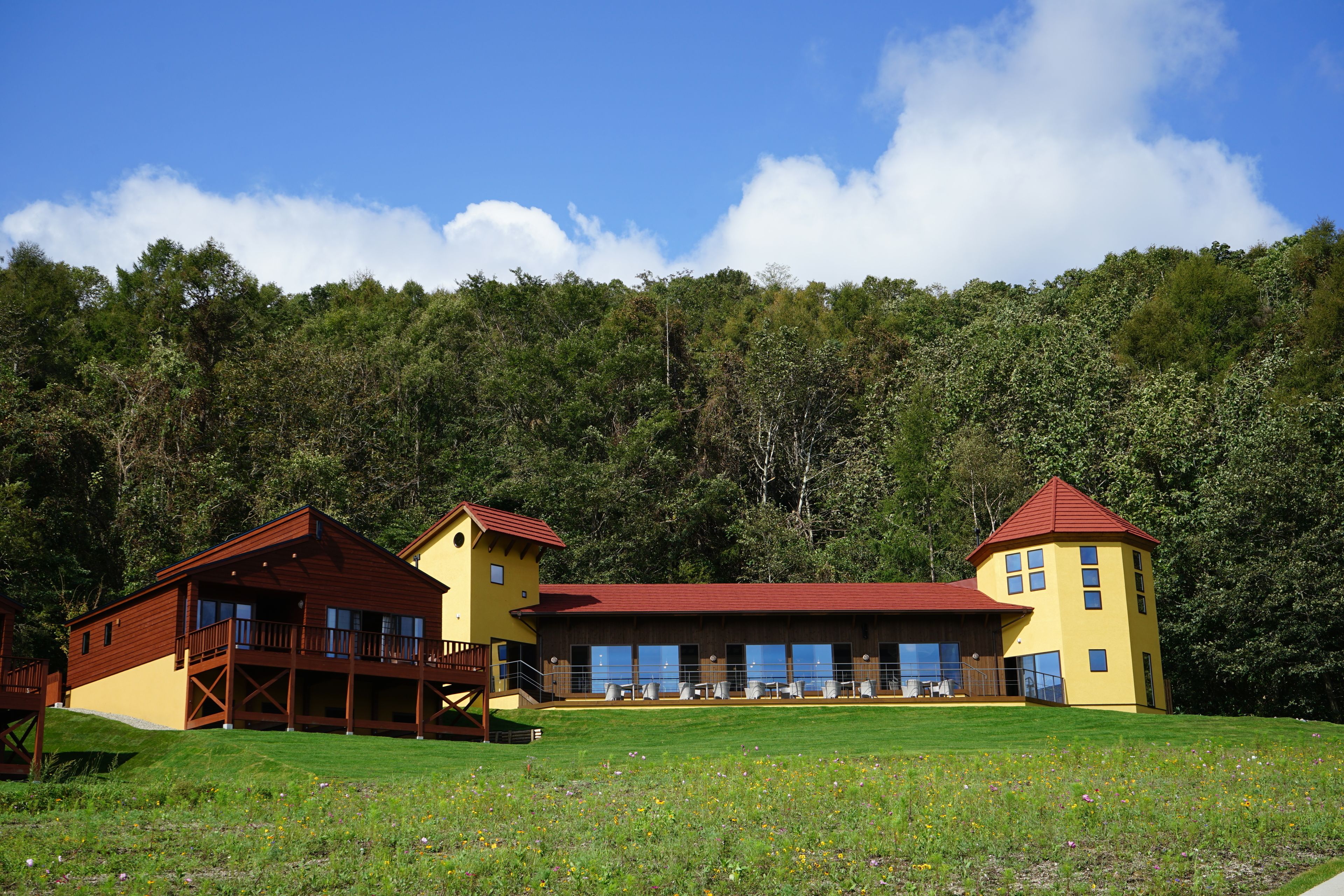 A two-story lodge with a red roof and yellow walls, featuring a large deck and multiple windows.