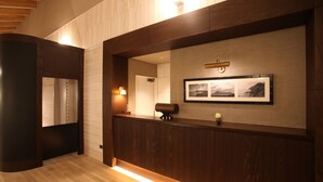 A reception area with a wooden reception desk, a framed photograph on the wall, and a mirror above the desk. - Hills Terrace Hakodate (Mori)
