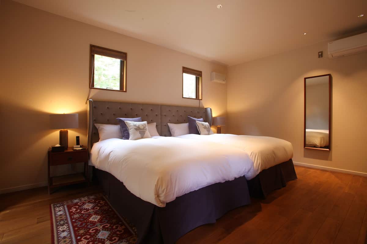 A bedroom with a large bed, a nightstand, a bedside table, a mirror, and a patterned rug.