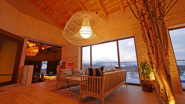 A spacious living area with a wooden ceiling, large windows, a wooden sofa, and a hanging light fixture. - Hills Terrace Hakodate (Mori)