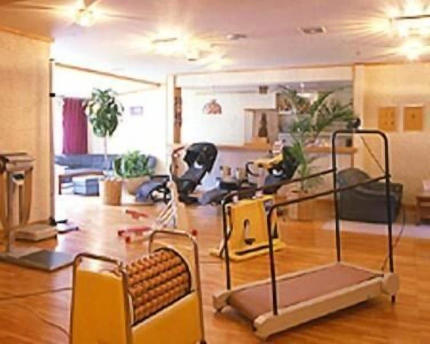 A spacious living area with a wooden floor, a sofa, a coffee table, and a dining table. There are potted plants and a baby stroller.